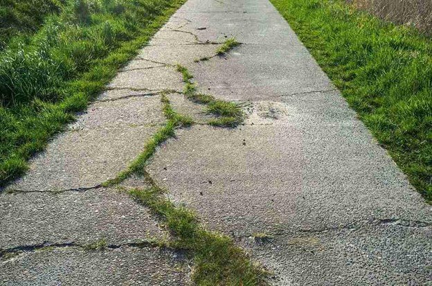 Cracked and damaged concrete driveway with visible wear and weeds growing through the surface in Eastlake, OH